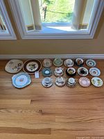 Wide shot of all teacups, saucers, and plates arranged on wooden floor under window with natural light, showing various colors and patterns.