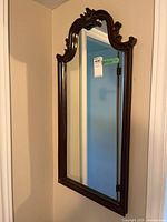 Full view of ornate wooden framed wall mirror showing curved top with intricate carved details and reflective glass.