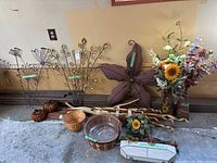 Full view of the wire and tin leaf themed wall decor, faux flower arrangements, glass pumpkins, wicker baskets, and other decor pieces arranged against a garage wall on concrete floor.