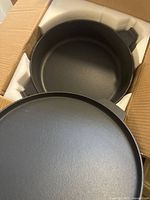 Top-down view of cast iron pot with lid inside original box and foam padding.