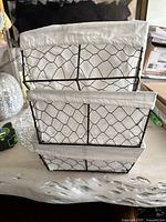 Three wire storage baskets stacked inside each other, showing black wire frame and white fabric liners.
