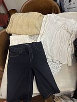 Dark blue denim jeans, white long sleeve shirt, and cream wool shawl on a table and chair.