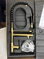 Faucet laid in foam packaging showing spiral spring neck, single handle, and spout with deck plate and flexible hose wrapped in plastic.