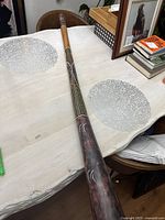 Full length view of the didgeridoo on a table showing natural wood mouthpiece and painted body with carved motifs.