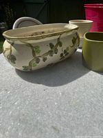 Garden pots on a white table outdoors showing the long ceramic planter with green raised vine leaves.