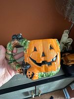 Close-up of Halloween pumpkin mug showing jack-o-lantern face, green vine handle with small black bats, and detailed orange finish.
