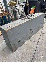 Closed handmade wooden chest with gray paint and leather handle, showing wear on edges.