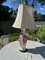 Front view of floral design ceramic lamp with beige fabric shade on outdoor table.