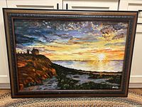 Full view of the original framed oil painting showing ocean sunset, rocky cliff, lighthouse and colorful sky.