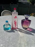Three perfume bottles displayed outdoors on a table in natural light showing their shape and branding