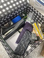 Open black and white checkered box with a black stapler, blue tape roll, two patterned fabric jewelry holders, note cards, and small items including a gray scrunchie.