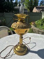 Full view of the vintage brass lamp, showing the entire lamp on a white table outdoors with a garden background.
