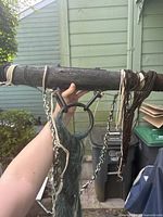 Close-up of the wooden pole with attached metal chains and textile materials showing detail and condition.