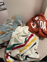 Three blankets on floor: Hudson’s Bay multistripe, Pendleton patterned, Ontario Canada rust red.