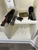 Group view of knives, multi-tools, sheaths on shelf