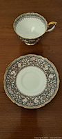 Photo of one bone china teacup and matching saucer with intricate floral and gold patterned design