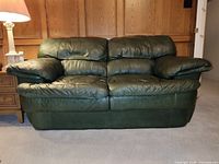 Front view of forest green leather sofa with two large seat cushions and padded armrests.