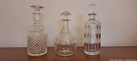 Front view of 3 different crystal decanters with stoppers, showing patterns and shapes