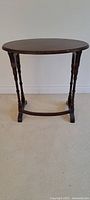Full view of dark brown wooden oval side table showing oval top and turned legs with curved stretcher base.