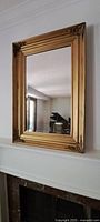 Full view of gold framed mirror mounted above fireplace mantle, showing frame details and room reflection