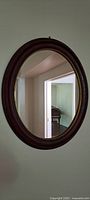 Front view of medium oval wall mirror hung on a beige wall showing reflection of a piano and doorway.