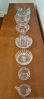 All crystal pieces lined up on wooden table showing their various sizes and cut designs, from large bowls to small plates and creamer