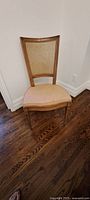 Single beige vintage wooden dining chair with cane backrest photographed on hardwood floor.