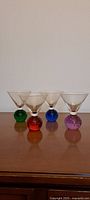 Front view of 4 vintage martini glasses in a row showing colored bubble bases of green, red, blue and purple.
