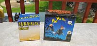 Photo showing two boxed Halloween decorations, a Shrieking Ghost and a witches flying decoration, outdoors on a table.