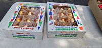 Two white boxes labeled 'Santa Land Christmas Tree Ornaments' each containing 12 gold-colored bulb ornaments arranged in a grid, shown on a light surface.