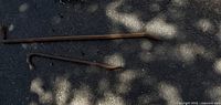 Photo showing two large crowbars lying on asphalt, with sun and shadow patterns. Both crowbars appear rusted and heavily used.
