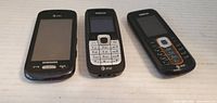 Photo showing three cellphones lying side by side: Samsung touchscreen phone, Nokia phone with white keypad and AT&T logo, Nokia phone with black and orange keypad.