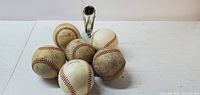 Six baseballs arranged in a small pile with visible scuff marks and dirt, alongside a small silver trophy.