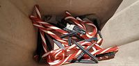 Box filled with 13 red and white striped light up candy cane decorations with black stakes, some wires visible, untested.