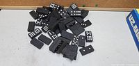 Pile of black domino pieces with white dots on a white surface, some dots showing various numbers including three, five, and six.
