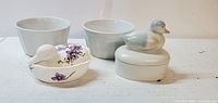 Photo showing two white ceramic bowls, one with scalloped edge, and two ceramic bird-shaped trinket boxes, one with purple floral decoration and the other with a blue and white bird lid.