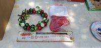 Photo showing a Christmas bell wreath, red Christmas stocking in packaging, and boxed 50-light Christmas set.