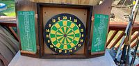 Front view of dart board mounted inside dark wood cabinet with open doors showing green scoring chalkboards.