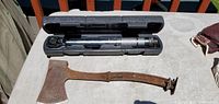 Photo showing large rusty hatchet and automatic torque wrench in case on table.