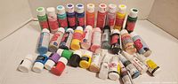 Photo 1 showing front view of multiple bottles of small acrylic paints in various colors arranged in rows.