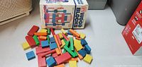 Multicolored wooden blocks scattered on floor with original box behind them