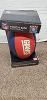 Front angled view of boxed youth size football showing New York Giants branding and NFL logos.