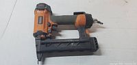 Front view of the Ridgid orange and black pneumatic nail gun lying flat showing the handle, trigger, and nail magazine.