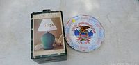 Photo showing boxed Pfaltzgraff table lamp next to the 200th Anniversary commemorative plate on a white surface.