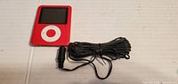 Red iPlayer digital media player with screen and white circular click wheel with attached charger cable
