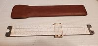 Slide rule laid out next to brown leather case, showing the length and design of the instrument