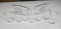 Six small clear glass beakers arranged in front of a clear glass candy dish with boat shape.