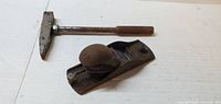 Photo of a small metal hand planer with knob handle, paired with a metal hammer with wooden handle, showing some rust and wear.