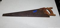 Hand saw lying flat with wooden handle and rusted blade visible from top angle.