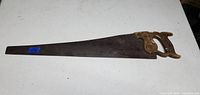 Photo of vintage handsaw showing full length, wooden handle on the right, blade spread out to the left with visible rust and patina.